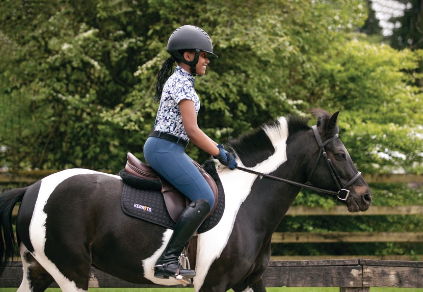 Girl riding a black paint pony while wearing the Kerrits Kids' Ice Fil Tech Tights in navy and a floral shirt.