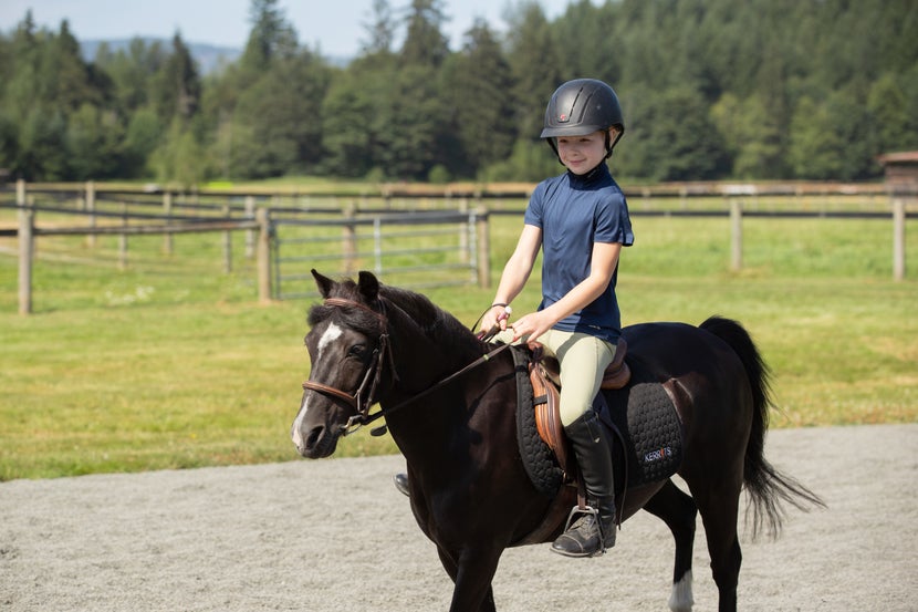 Child riding her little black pony, wearing a navy shirt and the Kerrits Sprout Starter Tights in tan.