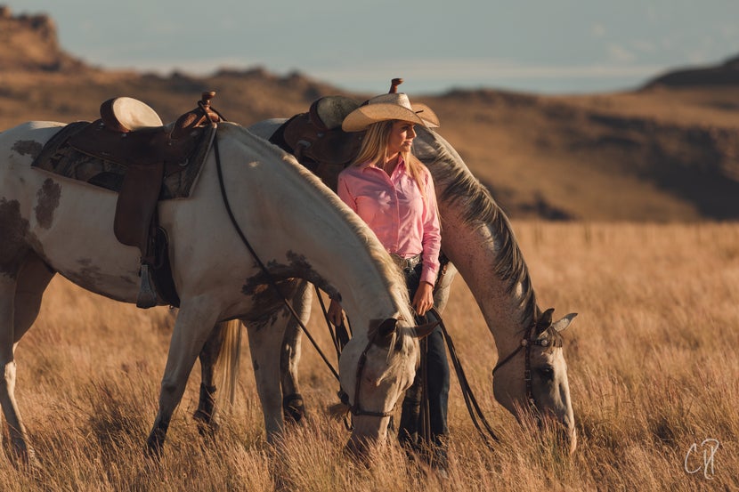 Renae stanidng in field with two of her horses in hand, grazing. 