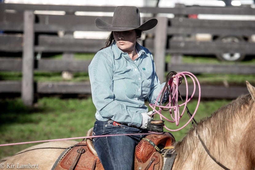 Woman on horseback with rope dallied on her saddle horn. 