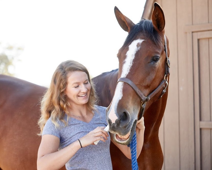 A woman feeding her horse an electrolyte paste.