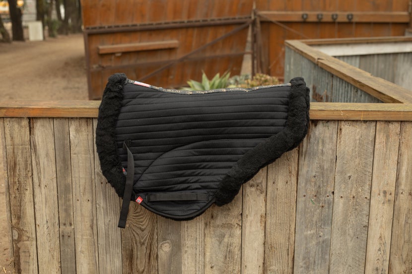 A Toklat T3 Endurance Coolback Saddle Pad sitting on top of a wooden fence. 