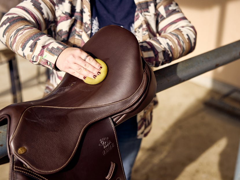Rider cleaning an English brown leather saddle with a sponge and saddle soap.
