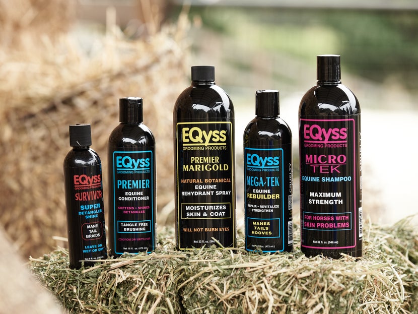 Eqyss bottles lined up on a hay bale, including: Marigold spray, Meg-Tek rebuilder, Micro-Tek shampoo, Premier conditioner, and Survivor super detangle shine.