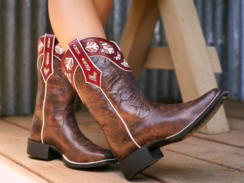Girl wearing cowboy boots with a square toe and red trim along the shaft. 