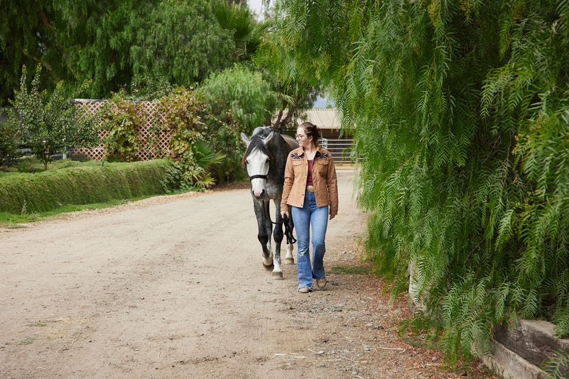 girl and grey horse walking along a path.