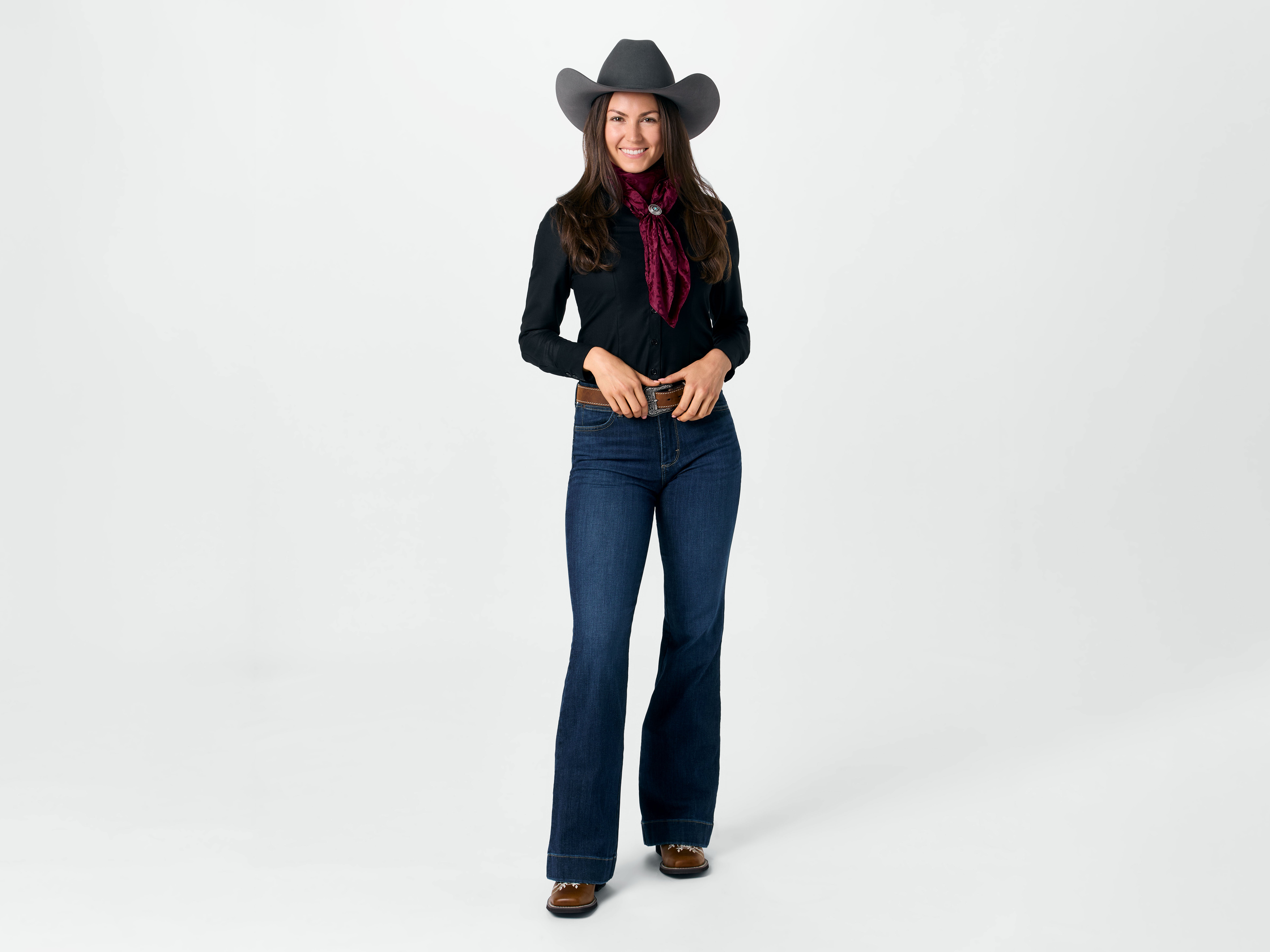 A lady wearing elegantly embroidered cowboy boots with a black western button downt shirt, dark wash trouser jeans, and a grey cowboy hat for an evening look.