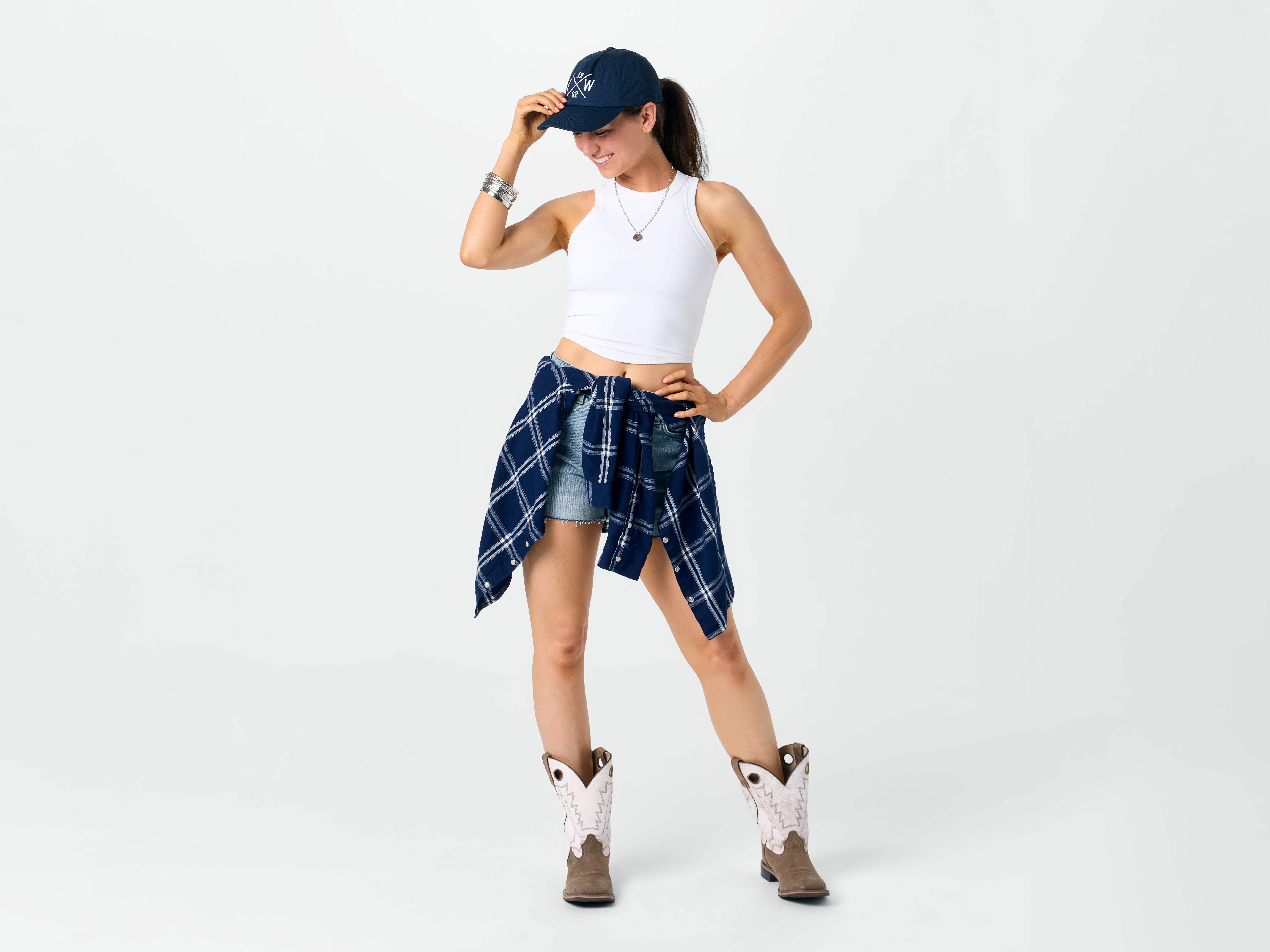 Lady wearing casual cowboy boots styled with jean shorts and a flannel shirt tied around her waist. 