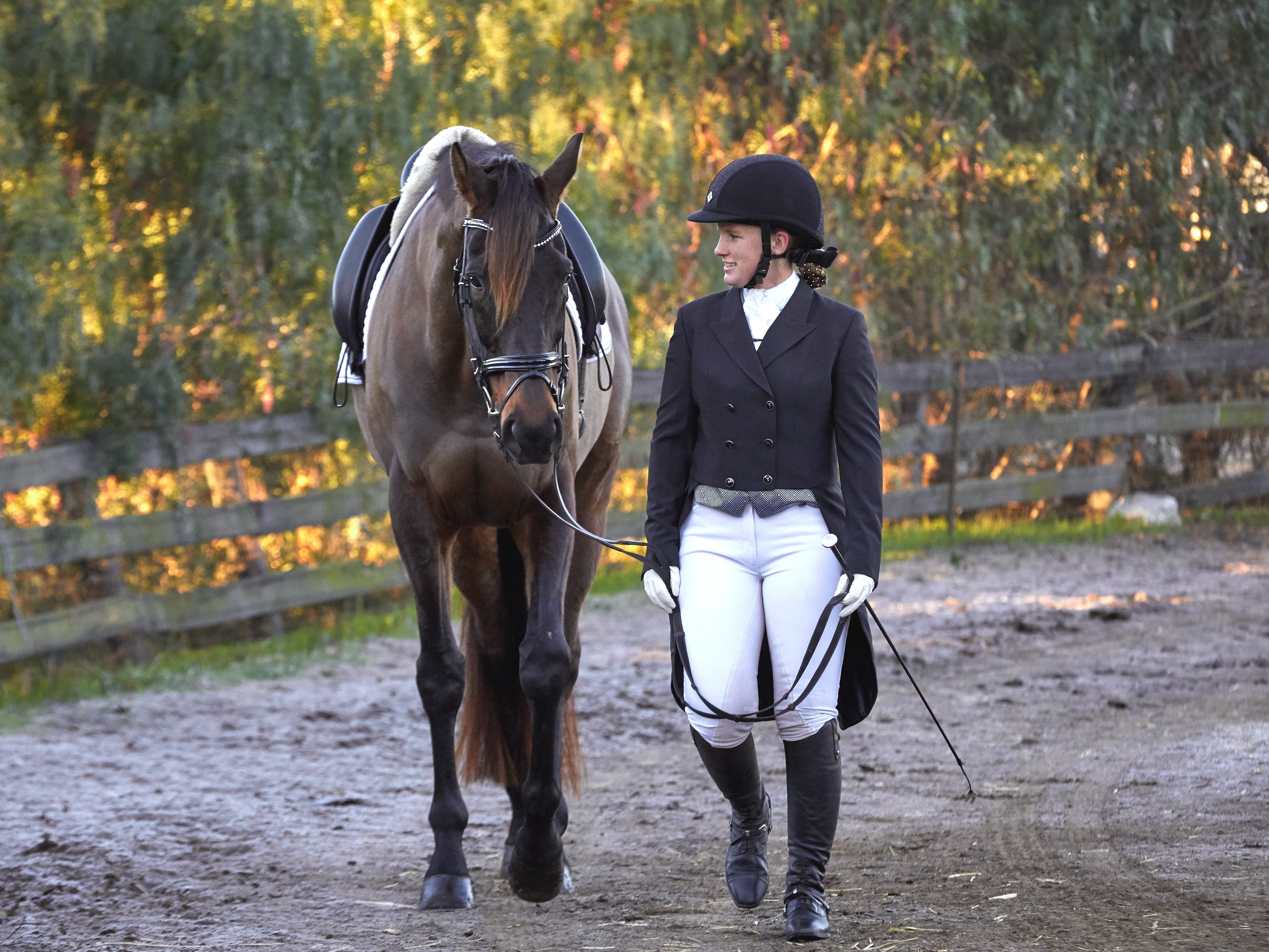 A women walking next to her bay horse, wearing a black shadbelly dressage coat.