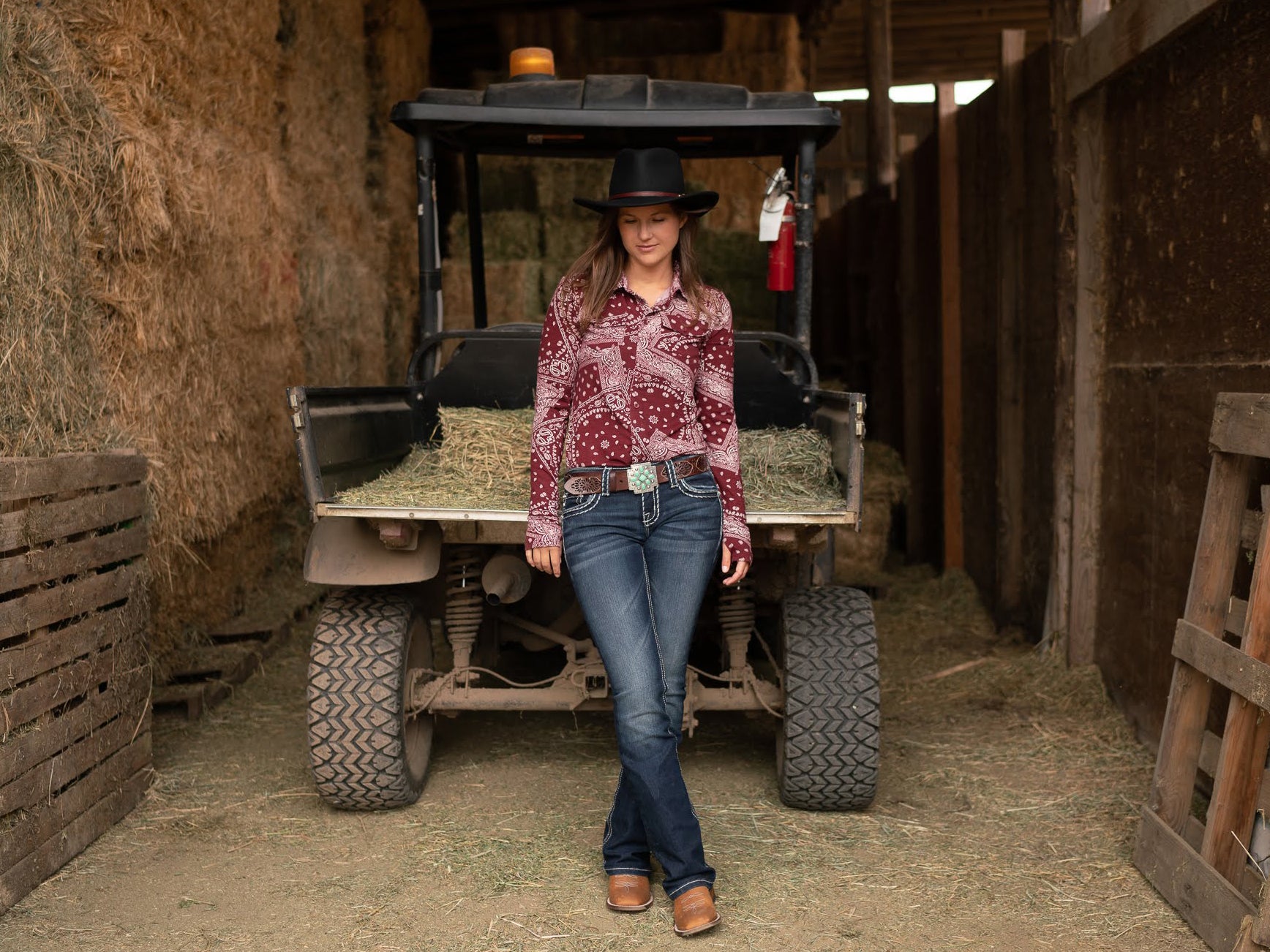 A women standing in front of a golf cart, wearing a button down shirt with a bootcut jean. 