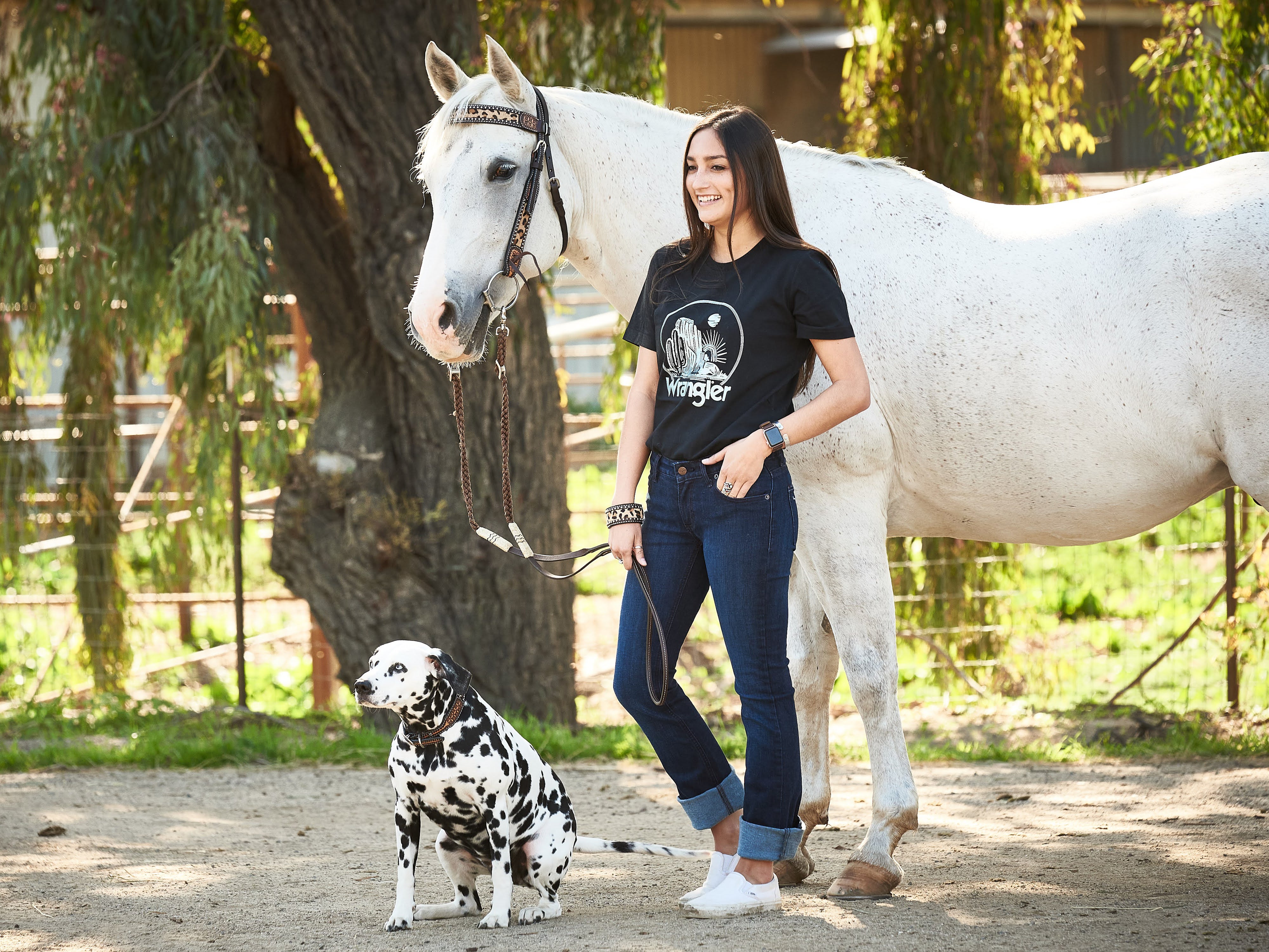 A women standing next to a grey horse and Dalmatian dog.
