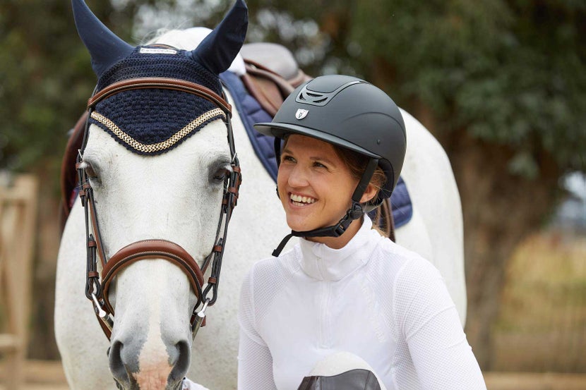 Equestrian standing next to a horse, wearing a riding helmet.