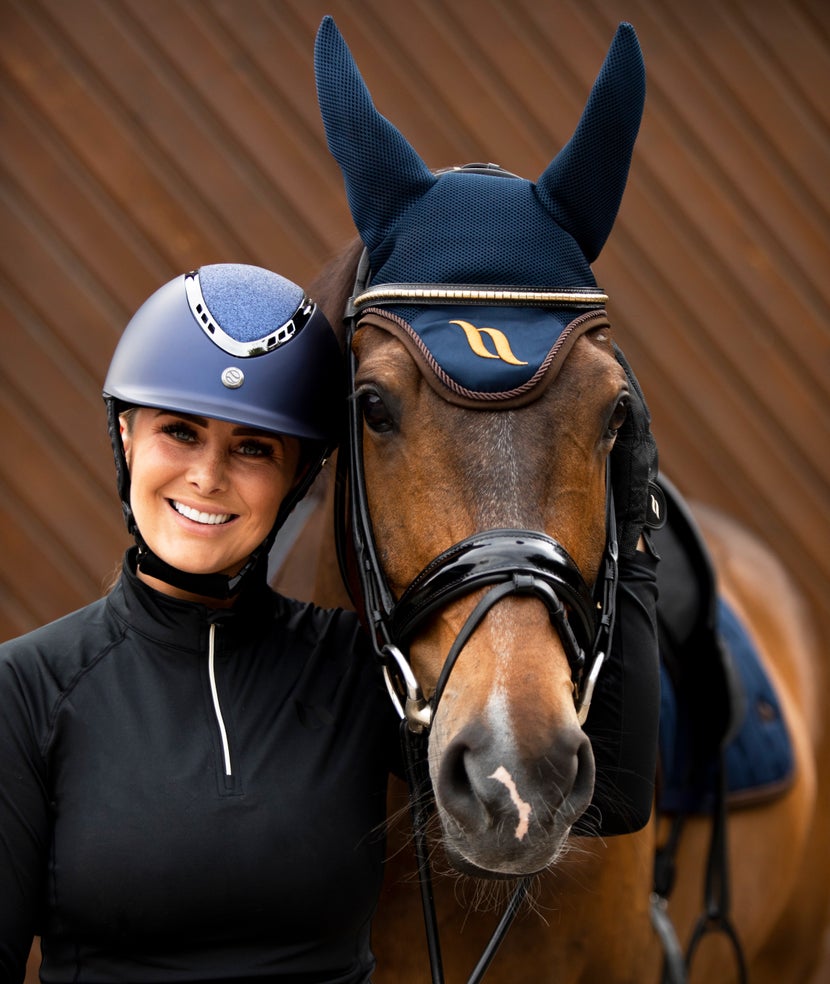 women wearing Trauma Void helmet standing next to a bay horse wearing Back on Track Airflow ear bonnet in navy with brown trim. 