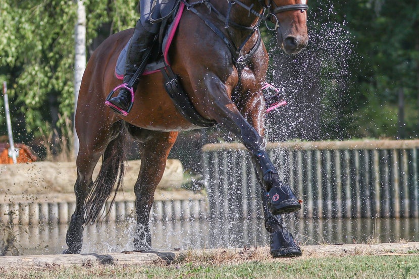 Rider cantering horse away from jump, with Equine Fusion hoof boots on.