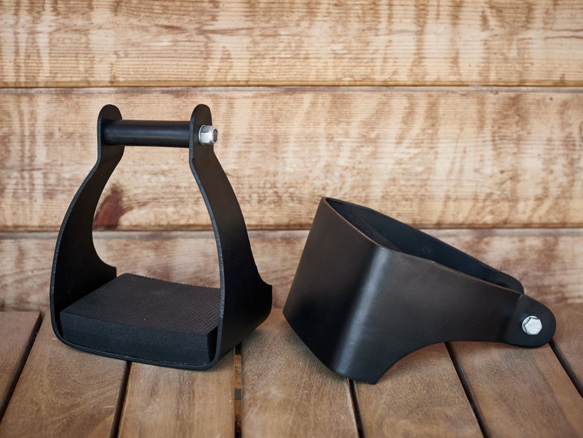 The Tough 1 Angled Aluminum Endurance Trail Stirrups sitting on a wodden floor against a wooden barn. 