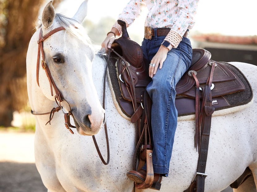 A cropped image of a rider sitting in a western saddle on her white horse. 
