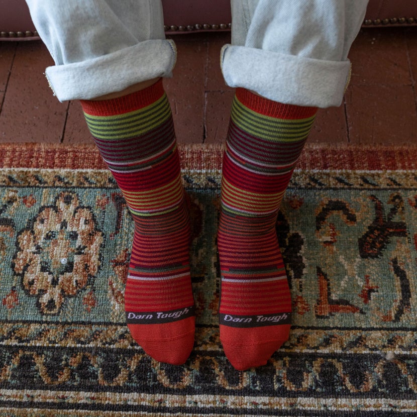 Downward view of a woman in sweats standing on carpet, wearing Darn Tough crew socks. 