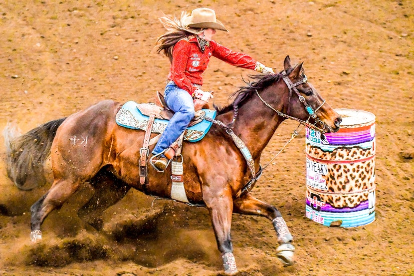 Krista at a barrel racing competition, turning around a barrel on a bay horse. 