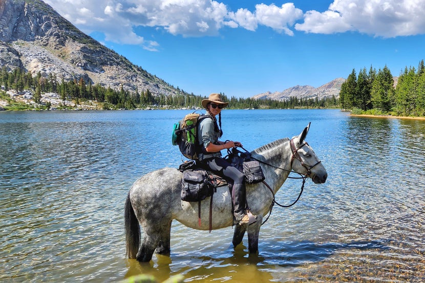 Gillian on her mule, Karlee, standing in a lake below the mountains. 