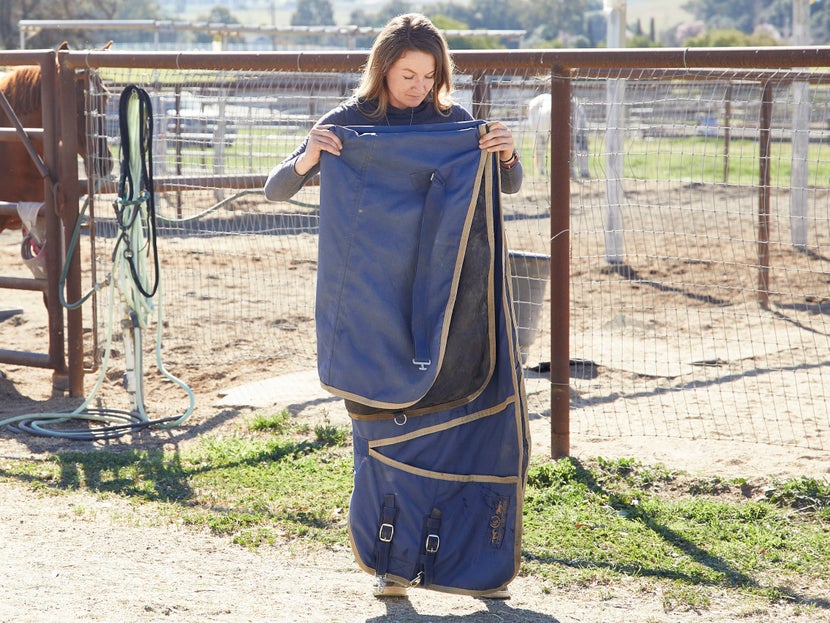 A girl folding a blue horse turnout blanket for storage. 