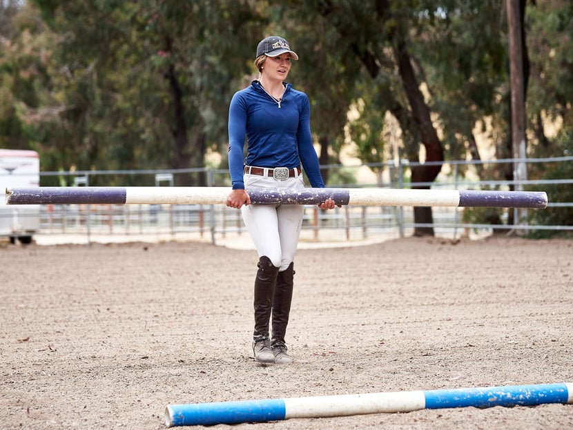 Girl carrying a a purple and white pole to place it in her jumping exercise.