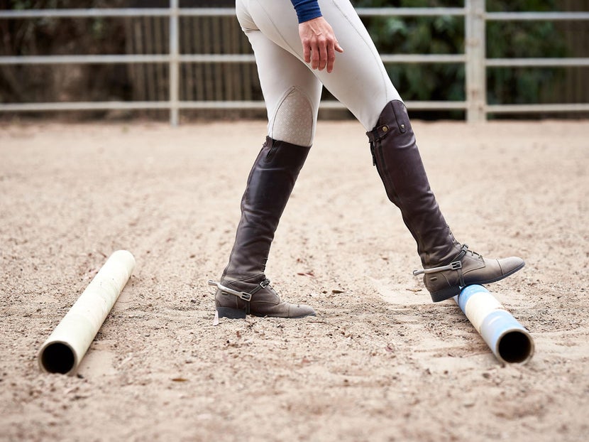Unmounted rider rolling ground poles with their feet to slightly adjust the distance. 