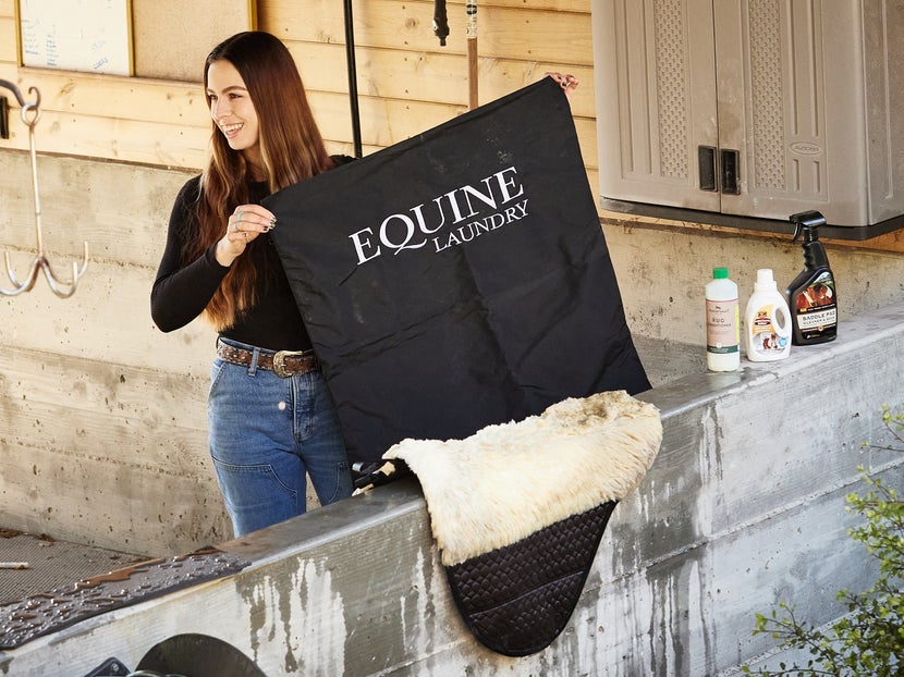 Woman holding up LeMieux equine laundry bag, with saddle pad and washing products. 