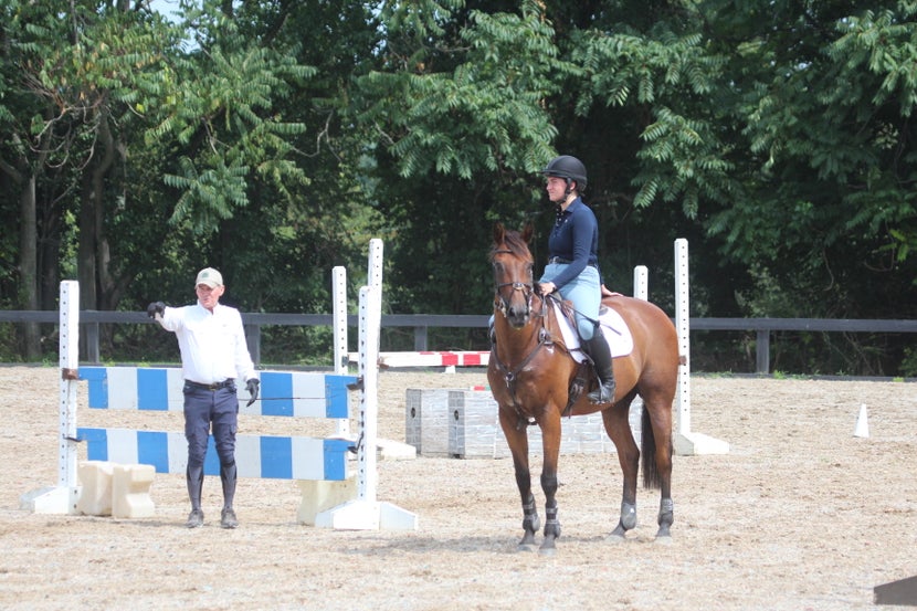 Stephen standing in arena next to a jump, talking with a woman on horseback. 
