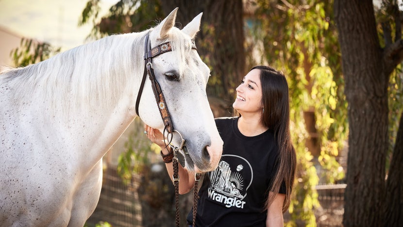 girl standing next to a grey horse wearing a western headstall